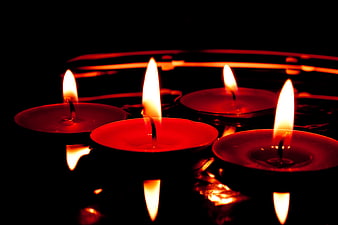 Red floating tea light candles with reflections in dark water
