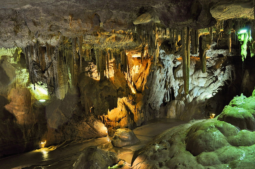 Illuminated limestone cave with stalactites and underground stream