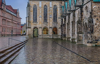 Wet cobblestone square with historic church and pink building