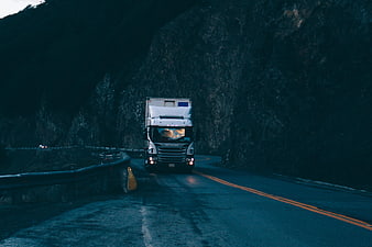 White Scania truck driving on winding mountain road at dusk