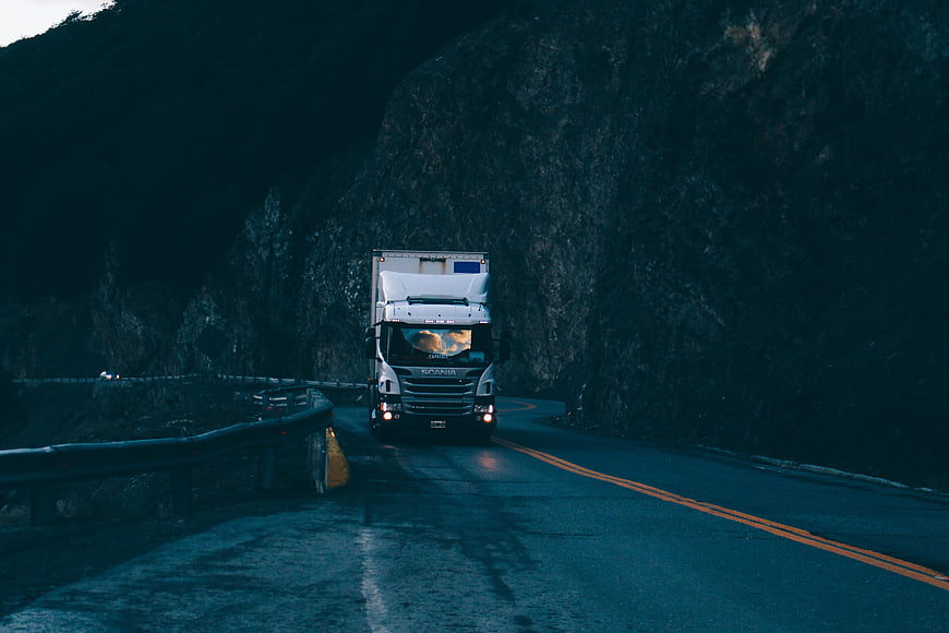 White Scania truck driving on winding mountain road at dusk