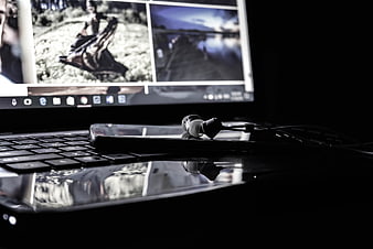 Laptop with smartphone and earphones in dark workspace