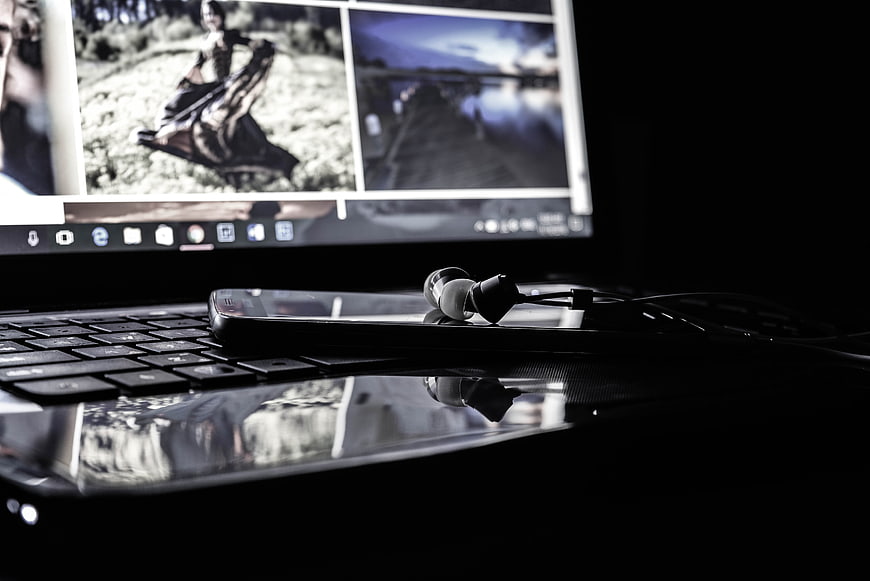 Laptop with smartphone and earphones in dark workspace