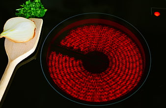 Glowing red electric ceramic hob with wooden spoon and onion