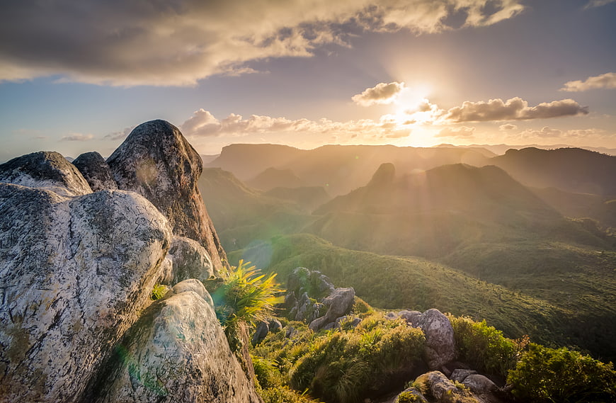 Sunset rays over rocky mountain peaks and green valleys