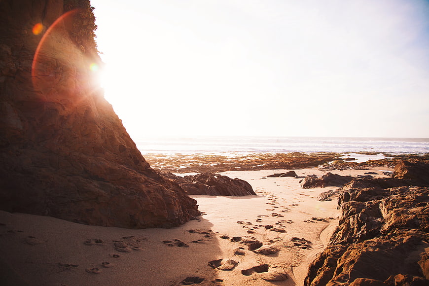 Sunlit Rocky Beach with Footprints and Ocean Horizon