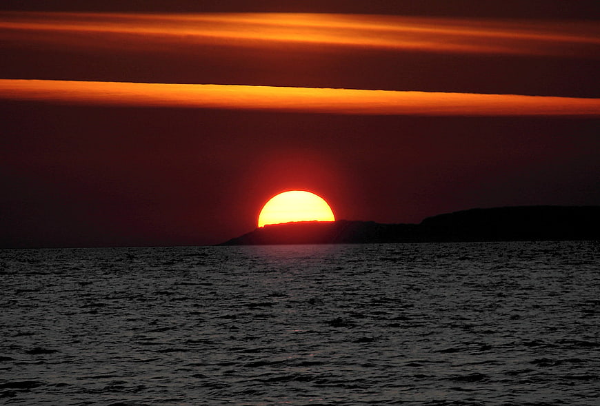 Vibrant orange sunset over dark ocean with silhouetted island