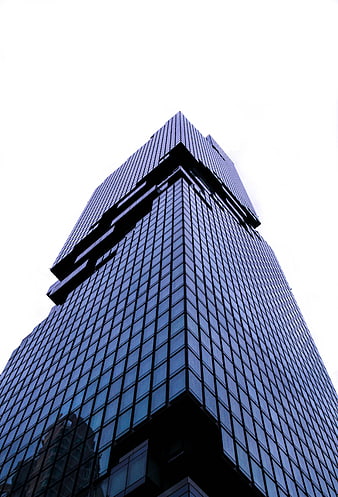Low angle view of modern glass skyscraper corner against white sky