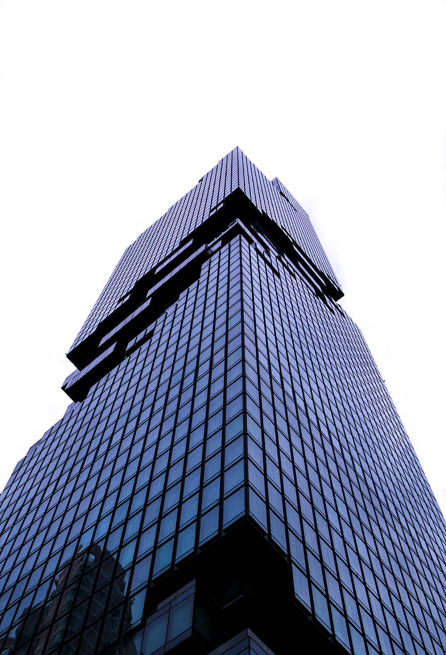 Low angle view of modern glass skyscraper corner against white sky