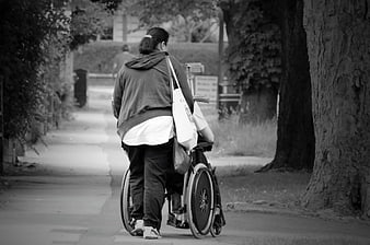 Senior woman pushing wheelchair on tree-lined street