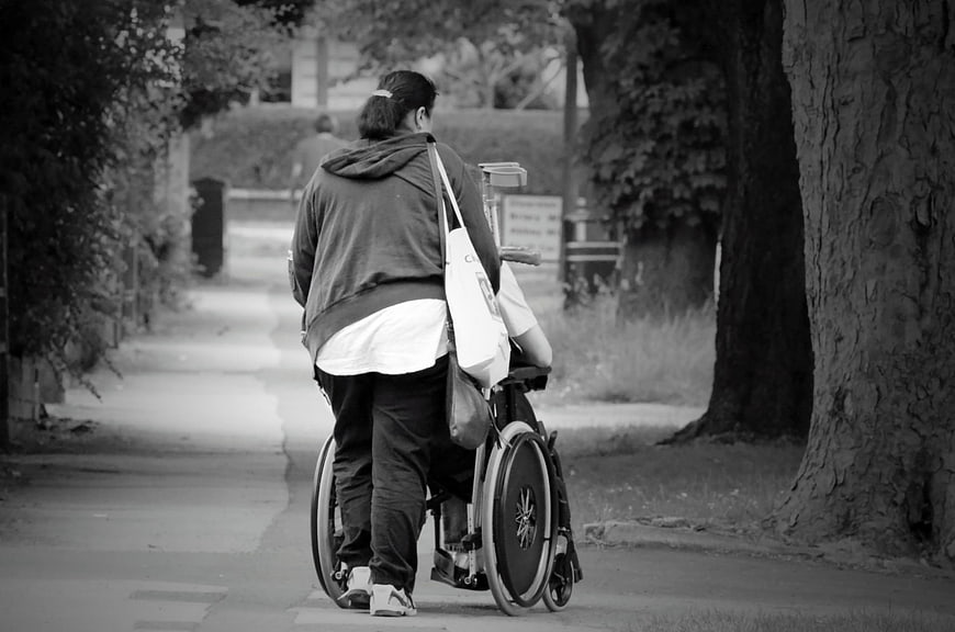 Senior woman pushing wheelchair on tree-lined street