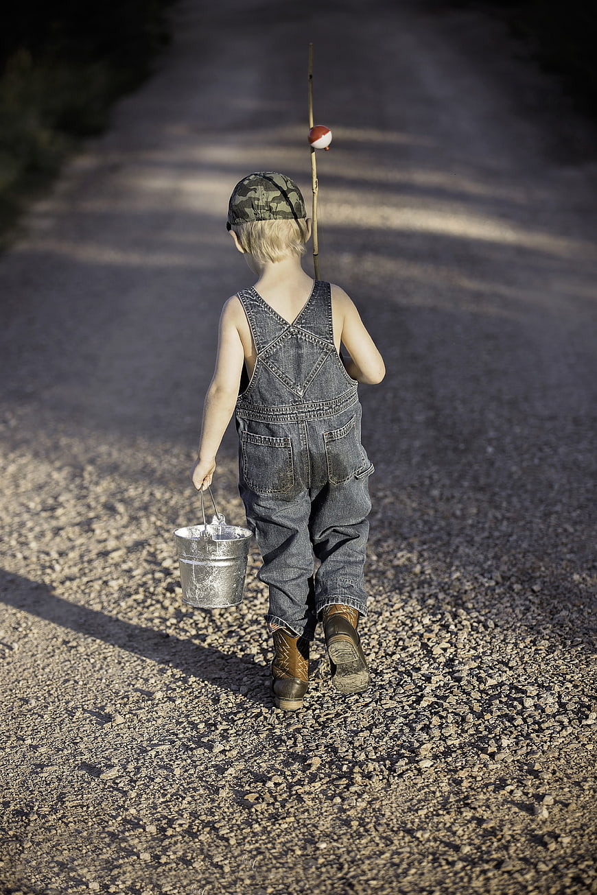 Little boy walking away with fishing bucket and stick