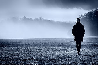 Silhouette of a woman walking in a foggy winter field at dawn