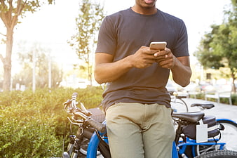 Man using smartphone next to blue bicycle outdoors