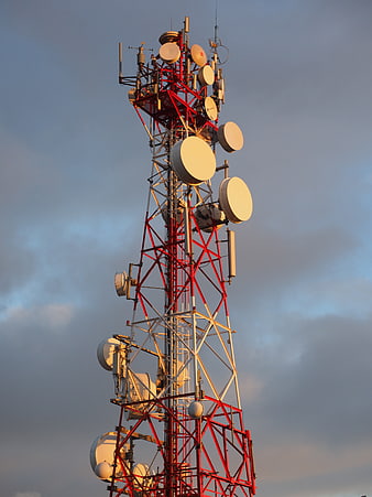 Red and white telecommunications tower with antennas against cloudy sky