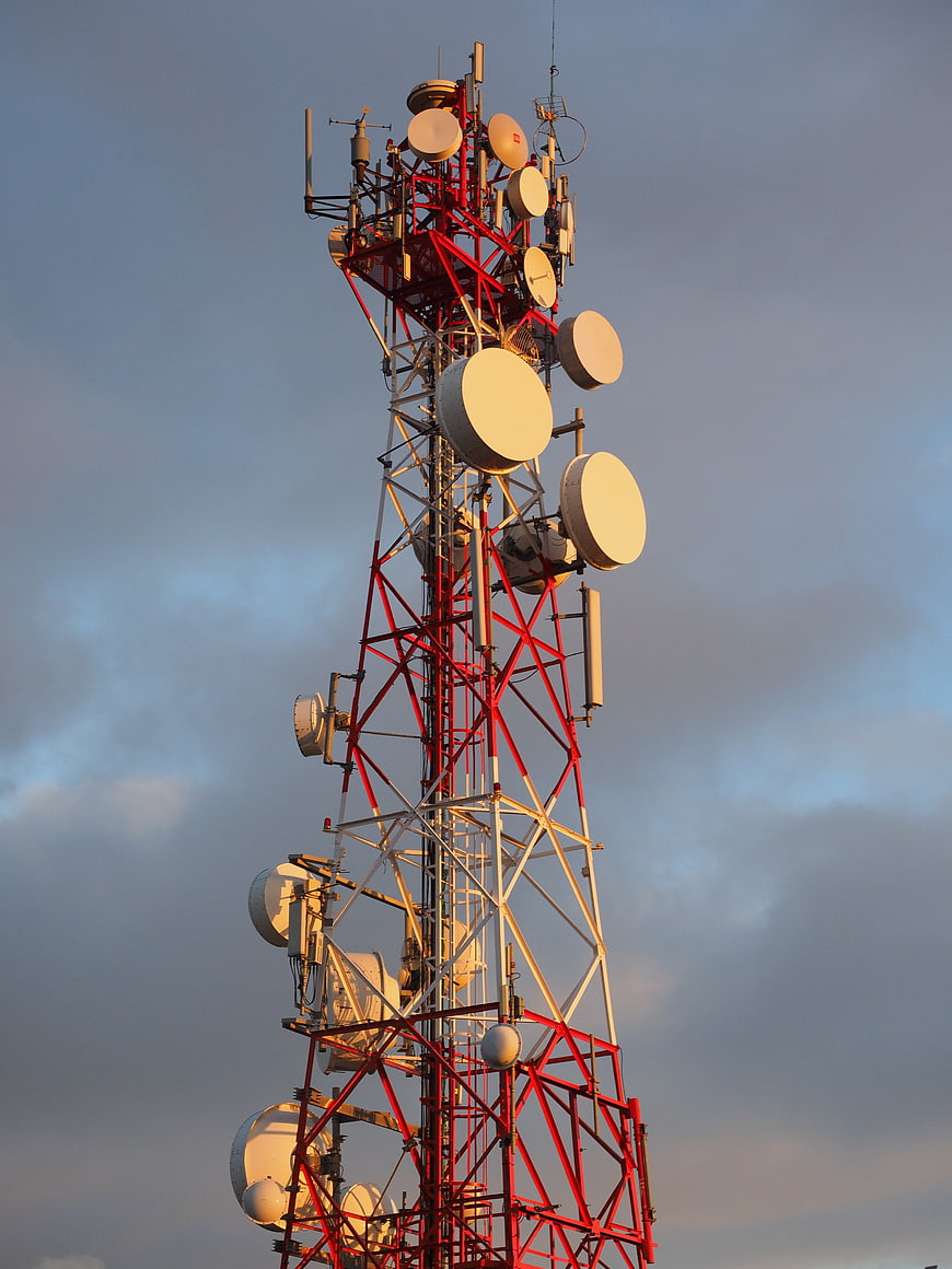 Red and white telecommunications tower with antennas against cloudy sky