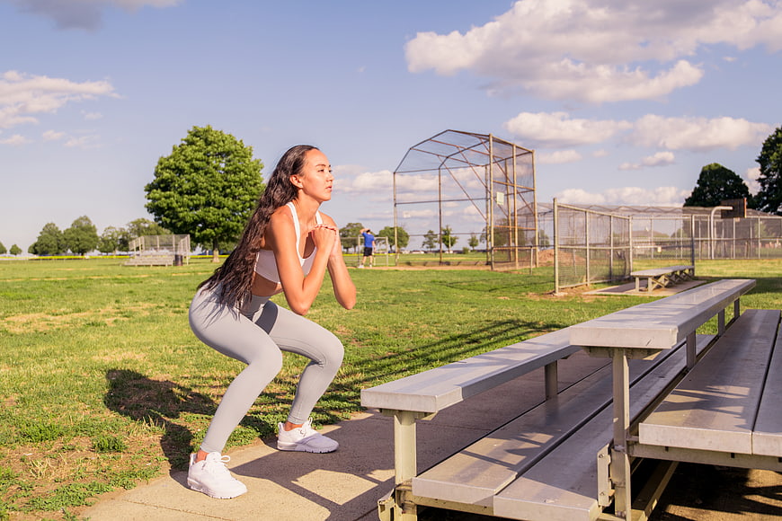 Woman performing squat exercise at outdoor baseball field