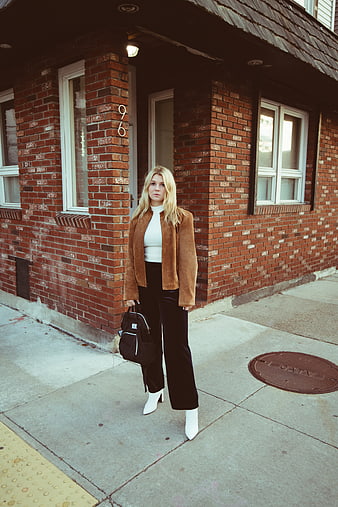 Stylish blonde woman in brown jacket standing on urban sidewalk