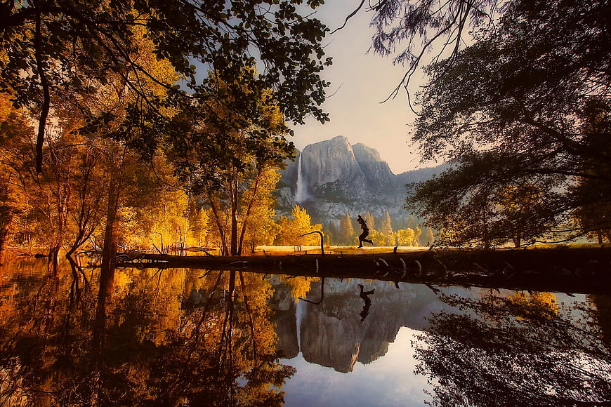 Man jumping on log with Yosemite Falls reflection