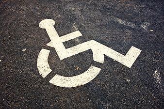 White Wheelchair Accessibility Symbol Painted On Textured Asphalt Road Surface