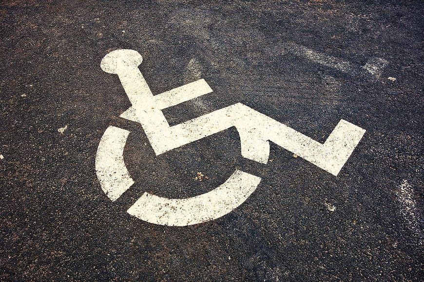 White Wheelchair Accessibility Symbol Painted On Textured Asphalt Road Surface