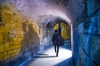 Musician with Guitar Case Walking Through Stone Tunnel