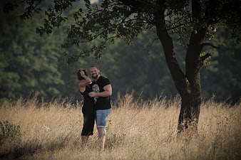 Happy couple embracing in a field of tall dry grass under a tree