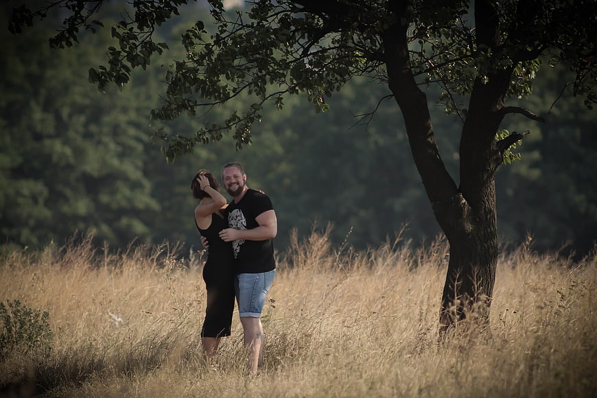 Happy couple embracing in a field of tall dry grass under a tree
