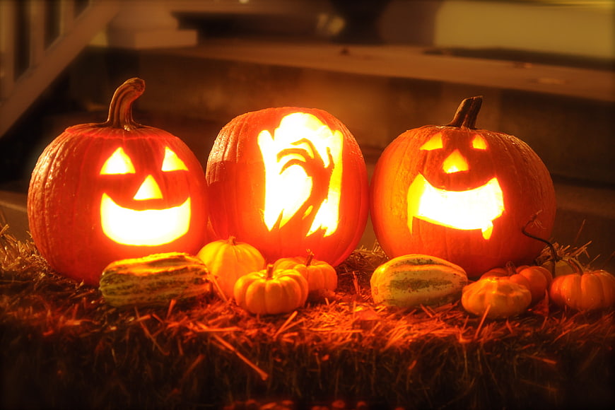 Three Glowing Carved Jack-O-Lanterns on Hay at Night