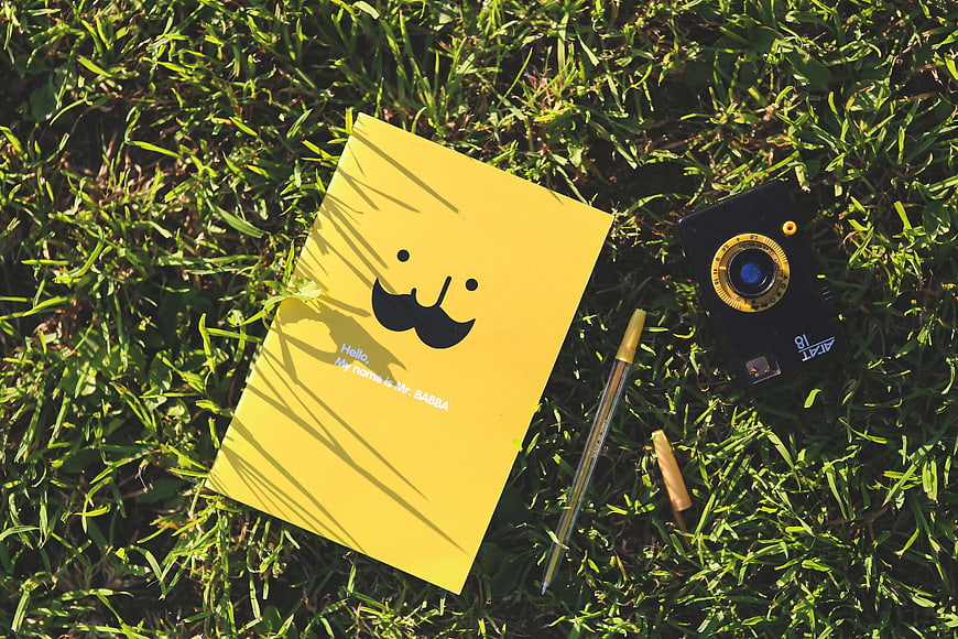 Yellow notebook and disposable camera on grass