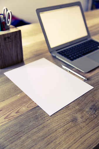 Minimalist workspace with laptop and blank paper on wooden desk
