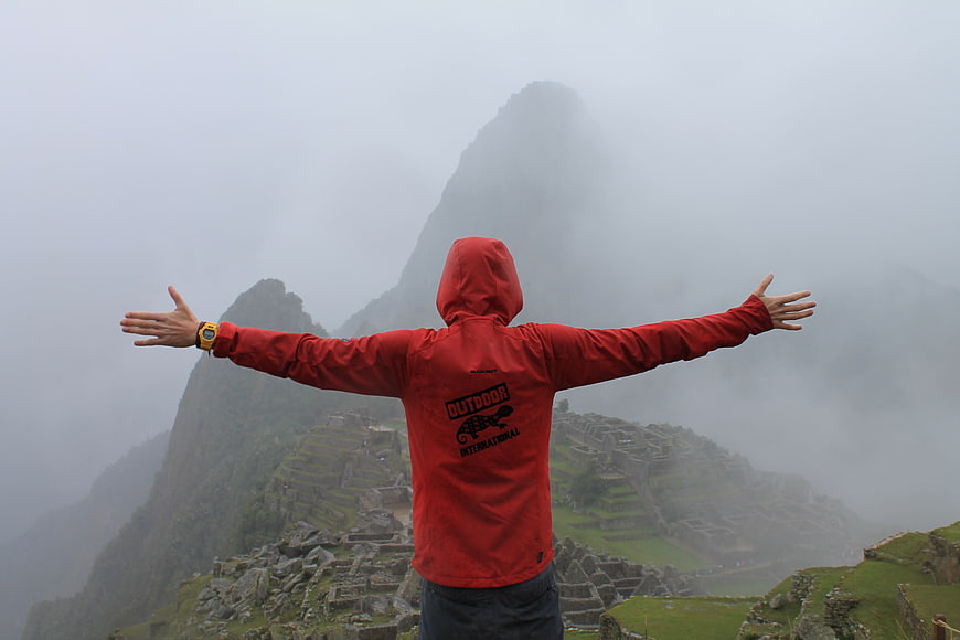 Man in Red Jacket with Arms Outstretched at Misty Machu Picchu