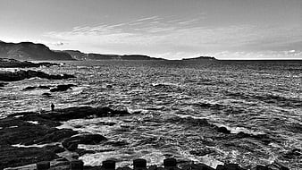 Black and white coastal landscape with rocky shore and distant mountains