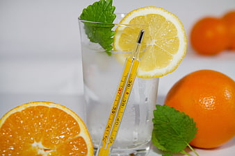 Glass of water with thermometer, lemon, and oranges for health