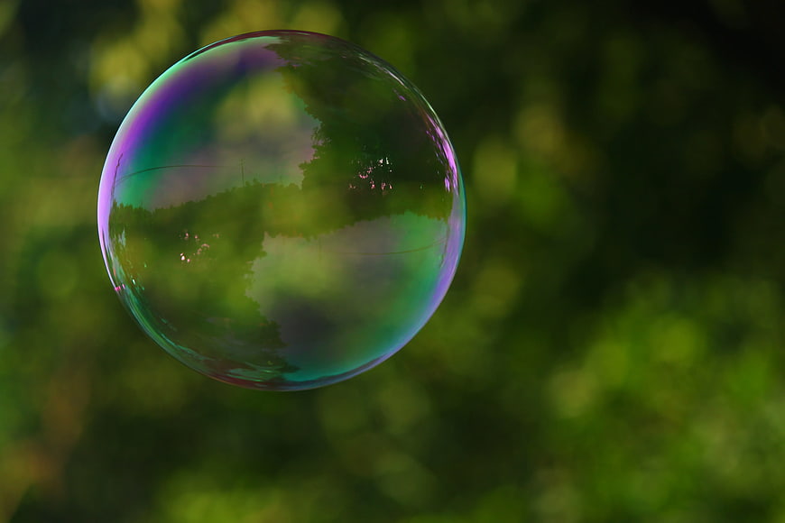 Iridescent Soap Bubble Floating Against Green Bokeh Background