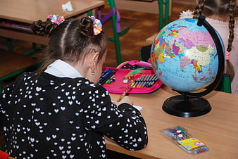 Schoolgirl Studying With Globe And Colored Pencils In Classroom