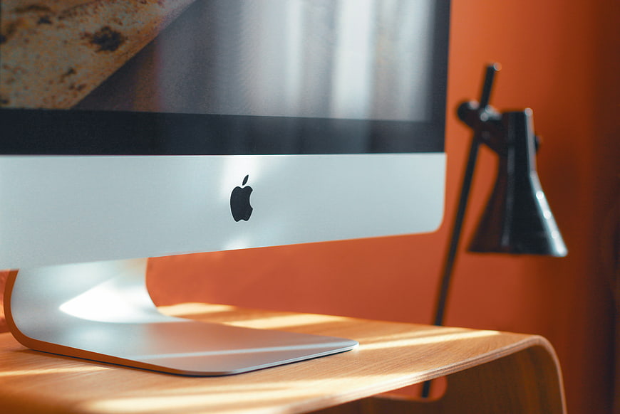 Close-up of Apple iMac on Wooden Desk with Orange Wall