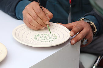 Hands painting green leaf pattern on ceramic plate