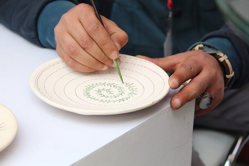 Hands painting green leaf pattern on ceramic plate