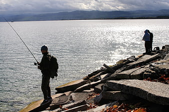 Fishermen on rocky shore with lake and mountains