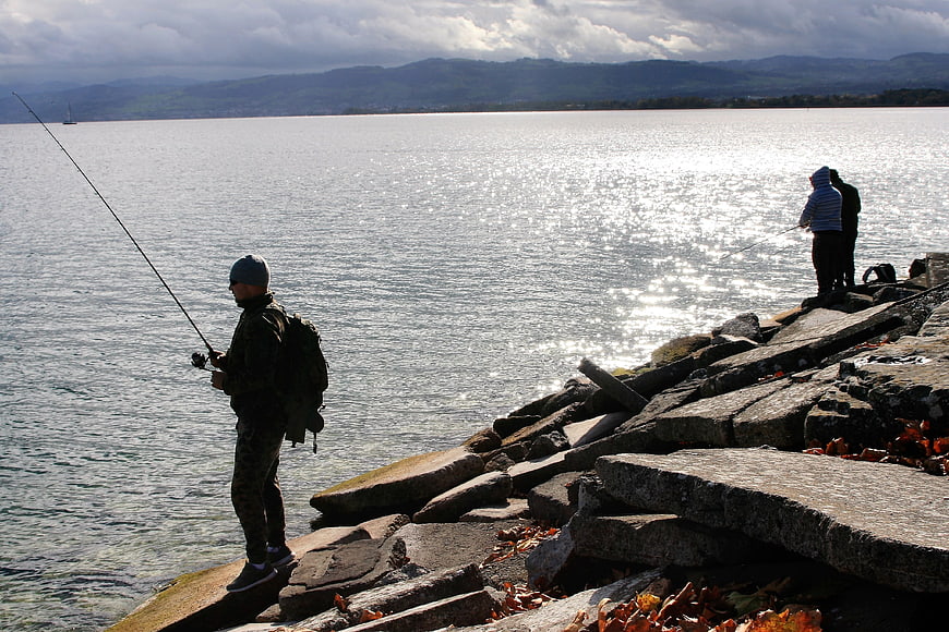 Fishermen on rocky shore with lake and mountains