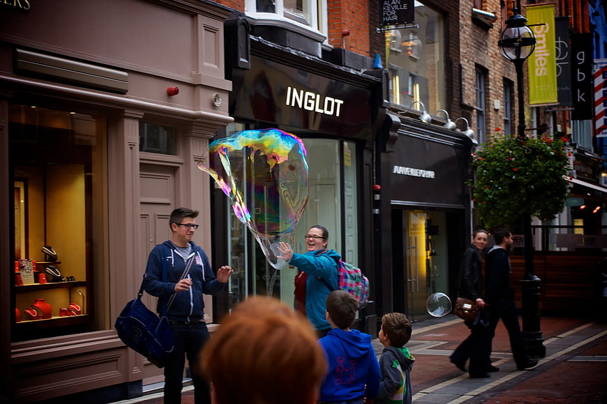 Woman Creating Giant Soap Bubble on City Street