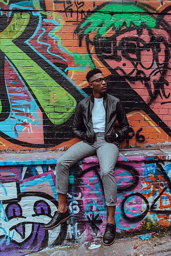 Stylish Man Sitting Against Colorful Graffiti Wall