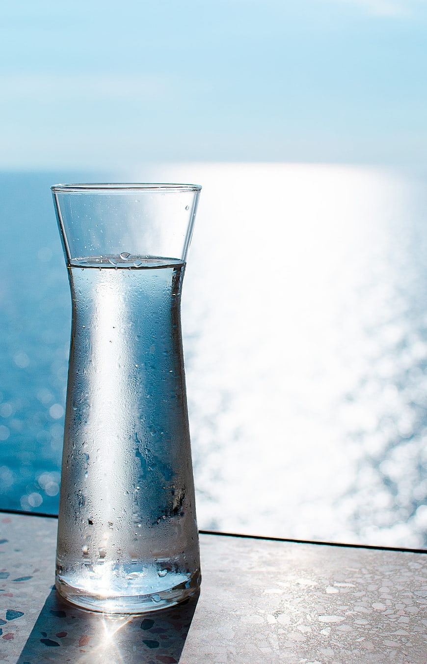 Condensed Glass Carafe of Water on Terrazzo Table with Ocean View