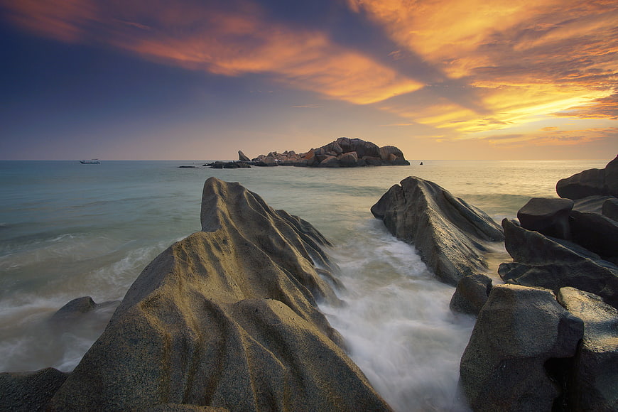 Dramatic Sunset Over Rocky Coastline with Smooth Ocean Waves