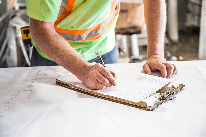 Construction worker writing on clipboard over blueprints