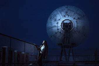 Woman standing on rooftop next to large satellite dish at night