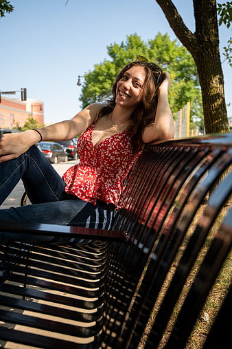 Smiling Young Woman Sitting on Park Bench in Sunlight