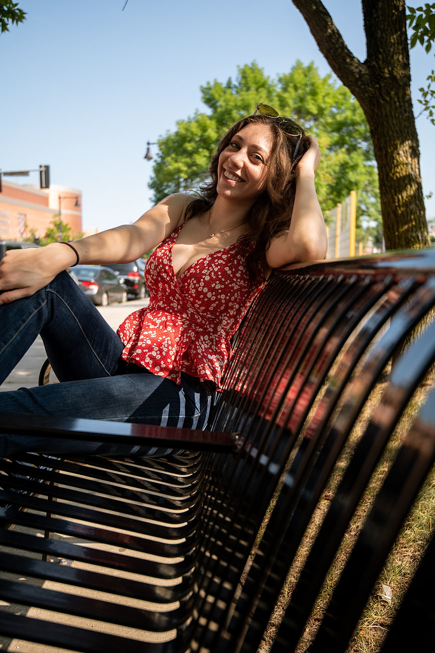 Smiling Young Woman Sitting on Park Bench in Sunlight