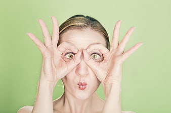 Playful young woman making funny face with hands on green background
